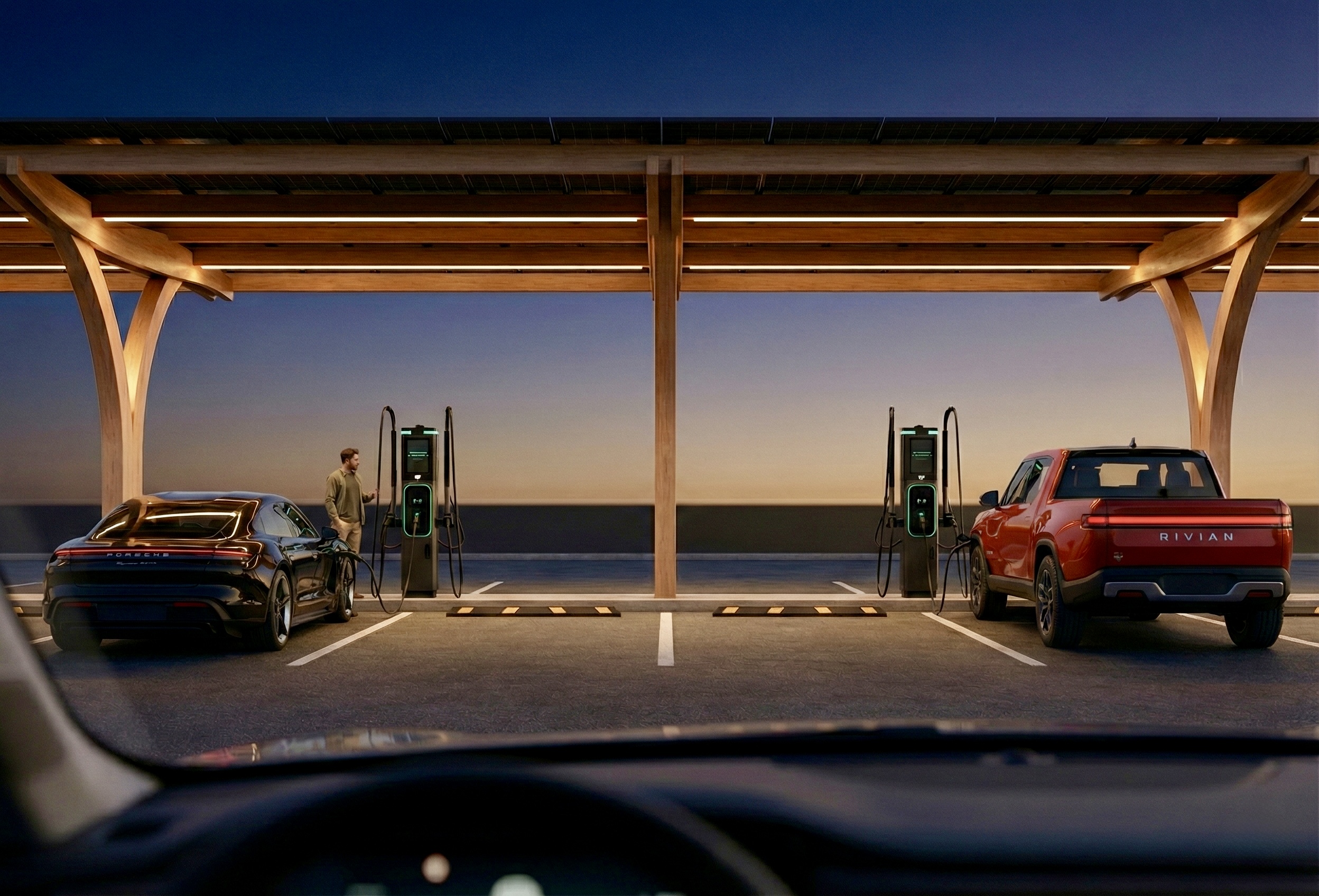 A Trailhead wooden canopy at dusk with two vehicles charging